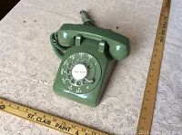 Front view of vintage green rotary phone with dial and cord next to rulers for size.