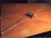 Full view of the fishing rod placed on a wooden table showing wooden handle and reel attachment.