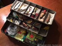Open metal tackle box showing multiple compartments filled with fishing lures and accessories
