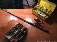 Fishing rod lying flat with two tackle boxes open beside it showing various lures and weights