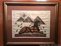 Full view of framed Egyptian papyrus paper art with sphinx, pyramids, and sun.