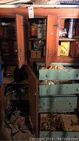 Wooden cabinets and drawers opened showing older power tools, household items, and cluttered storage space.
