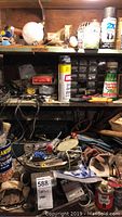 Shelf with aerosol spray cans, small parts organizer, Turtle Wax can, and various tools scattered below