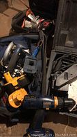 Photo showing multiple power tools and cases together including a blue cordless drill with yellow battery, a yellow power tool, and other tools in cases.