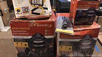 Photo showing boxed Malibu low voltage cast metal landscape garden lights with product details on packaging in Spanish and English.