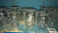 Multiple clear crystal glass pieces on shelves showing mixed stemmed and stemless glasses with detailed cut designs.