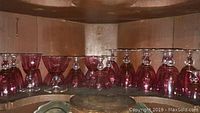 Shelf displaying fourteen cranberry glassware pieces with clear stems arranged upside down and right side up, various sizes and shapes visible.