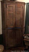 Full view of the tall corner cabinet showing upper and lower doors with medium brown finish, placed in corner of room.