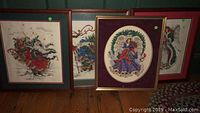 Four framed cross stitch Christmas scenes including two Santa Claus and two angels, displayed upright against wall