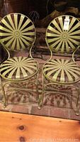 Front view of two metal outdoor chairs side by side showing sunburst pattern on backrest and seat, avocado green finish