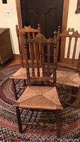 Photo showing three wooden chairs with vertical spindle backs and woven rush seats placed on a patterned rug in front of a wooden door.