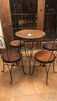 Full view of the cafe table and four chairs set on tiled floor, showing metal frames and wooden surfaces.