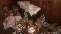 Photo of multiple dolls posed in a group, including a stroller with a cloth cover, cradle, and a bench in the background.