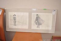 Framed watercolour artwork showing two distinct figures side-by-side, each holding a pole or rod, framed in one wide glass frame.