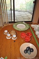 Full view of the lot on a wooden table near sliding glass door showing the teapot set, plate, marble eggs, and additional red cups.