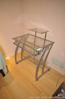 Front angle view of the tempered glass computer desk with curved silver metal frame and keyboard shelf.