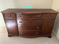 Front view of wooden dresser showing four curved front drawers with oval metal handles, two side cabinet doors with raised panels, and two small drawers above the cabinets, overall rectangular with slight curve in front.