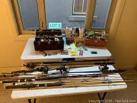 Full view of six fishing rods and reels with tackle boxes on a white folding table near a window