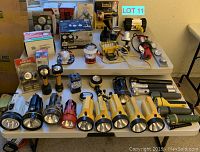 Full lot showing all flashlights, lanterns, work lights and boxed lighting items on white table and floor