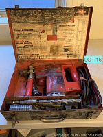 Full view of the open metal carrying case showing the power drill, drill bits, coiled cables, and accessories inside.