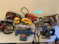Overview of eight corded handheld power tools on table against wall includes circular saw, jigsaws, sanders.