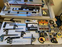 Overview of various measuring and layout tools arranged on a table including levels, rulers, squares, tape measures.