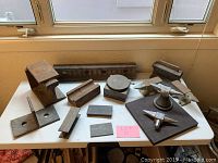 Wide view of lot showing anvils, railroad tie sections, metal mold parts, and assorted metal blocks and brackets on white table near window.