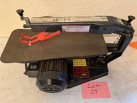 Side angled view showing the full scroll saw with black metal body, flat work table, and red blade guard attachment.