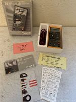 The Fluke 79 Series II multimeter in its original box with accessories including test leads, manuals, and quick reference sheets arranged around it.