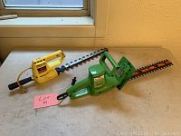 Two electric hedge trimmers placed on a table by a window, one green Sears brand and one yellow with black handle.