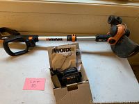 WORX cordless trimmer/edger with attached grass guard and adjustable handle placed on table. Comes with a 40V battery and charger in a box along with user manual.