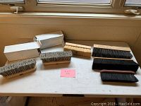 Seven assorted medium brushes arranged on a white table, including brushes with wooden and plastic bases, and various bristle colors.