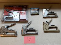 Full view of four staple guns and boxes of nails and staples arranged on a flat surface with label Lot 41.