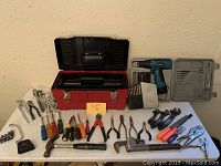 Full view of tool kit contents laid out on a surface with the red Stack On toolbox open at the back, cordless drill with case, and assorted hand tools in front.