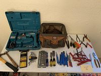 Wide view of all tools on white table including Makita drill in case, tool bag, hammer, screwdrivers, pliers, files, hex keys, and specialty pliers