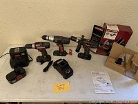 Lot displayed on white table surface showing three cordless Craftsman drills and battery chargers with batteries.