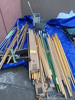 Overview of assortment of wooden mop handles on blue tarp with vintage galvanized mop bucket and wringer in background.