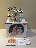 Ceramic house model placed on top of its original box, with two pamphlets in front.