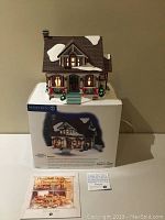 Front view of the Department 56 bungalow displayed on top of its original box with accompanying literature booklet in front.
