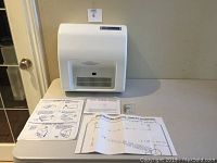 White wall mount automatic electric hand dryer with vent and sensor on front, along with mounting instructions, template and hardware next to it on a tiled floor.