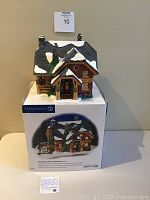 Front view of the ceramic Moonlight Bay Bunk and Breakfast building sitting on top of its original Department 56 box showing details of the roof, porch, chimney, and tree.