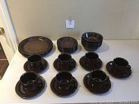 View of all dinnerware pieces arranged on table including plates, bowls, cups, and saucers in brown stoneware with decorative floral pattern.