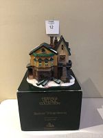 Front view of 'The Grapes Inn' miniature building atop its original green foam box with gold lettering from the Heritage Village Collection Dickens' Village Series.