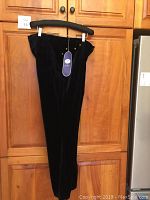 Full side view of navy blue DG2 Diane Gilman velour pants on wooden hanger showing overall shape and length.