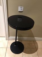 Full view of black round pedestal end table showing metal base and glass top