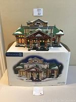 Front view of the Department 56 Village Train Station with warm lit windows on top of the original box showing the front and snowy details.