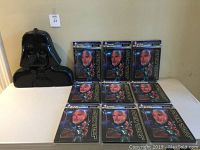 Darth Vader shaped black plastic carrying case and nine sealed Star Wars villain mousepads displayed on a white surface.