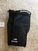 Black Bauer Supreme 1000 junior hockey pants laid flat showing full length and Bauer logos on the thigh and waist.