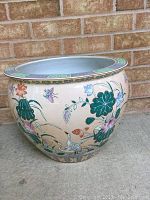 Full view of large porcelain planter pot showing floral and bird designs on light beige background with brick wall backdrop