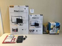 Lot items displayed on table including the BurCam Wi-Fi Water Watcher Alert box, TI-NSPIRE CX CAS calculator with cable, two Fellowes PrivaScreen privacy filter packages, and another smaller box for OtterBox phone case.